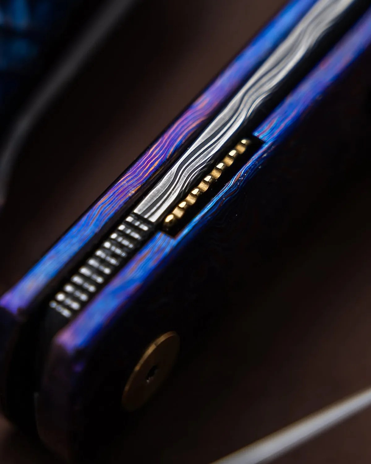 Close-up of a blue and purple patterned folding knife spine with visible metal liners and brass pins.