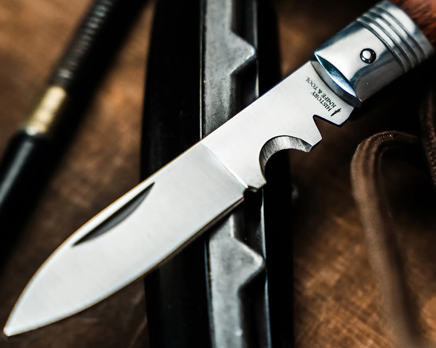 Close-up of a stainless steel knife blade with a wooden handle and "History Knife & Tool" engraved near the handle.