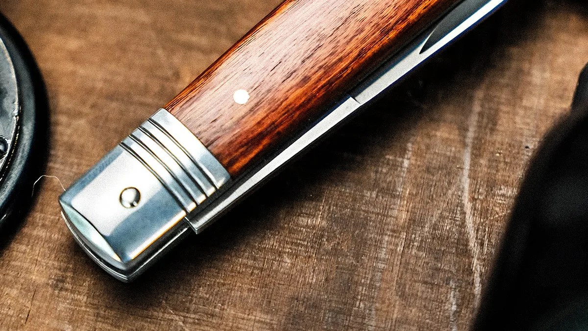 Close-up of a folding knife with a polished metal bolster and a wooden handle on a wooden surface.