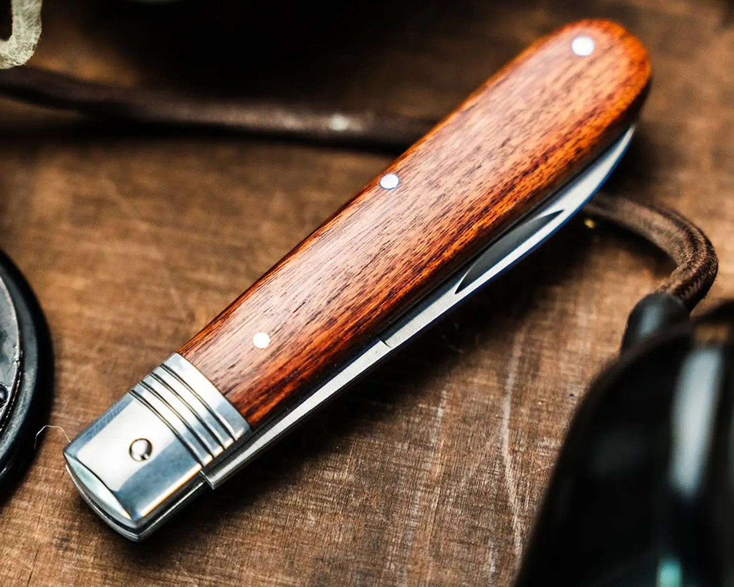Folding pocket knife with polished wooden handle and metal bolsters on a wooden surface.