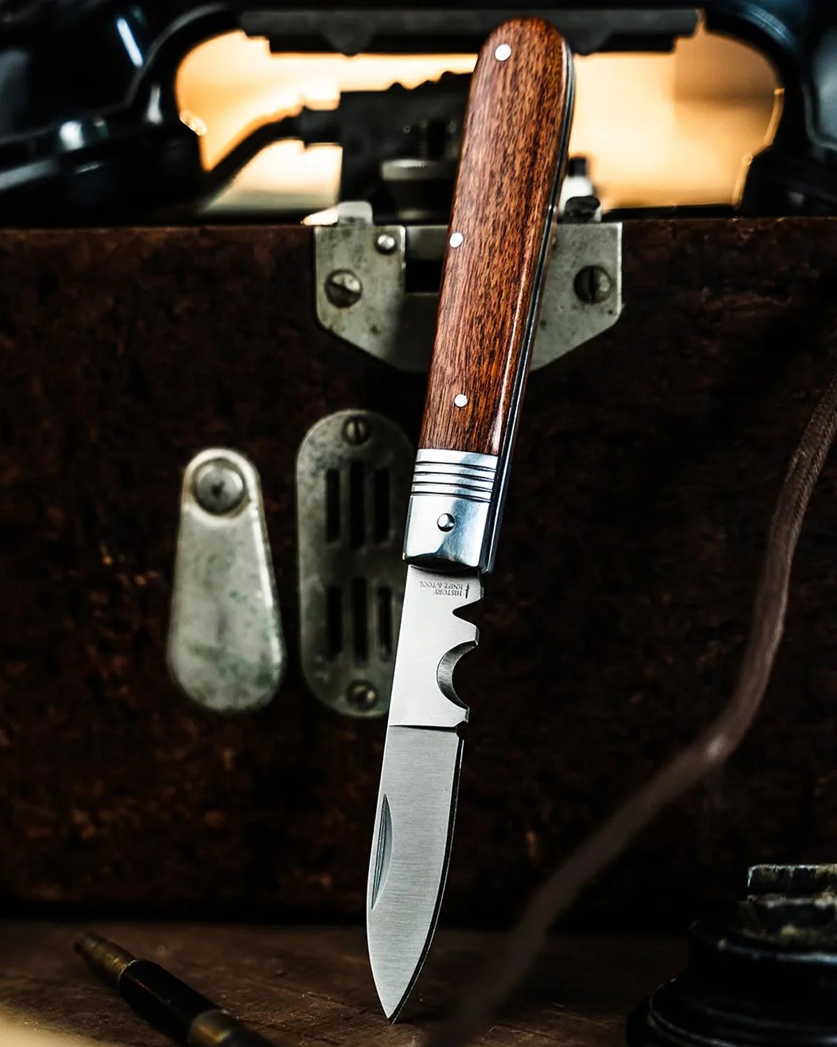 Folding knife with a wooden handle and a partially serrated stainless steel blade standing upright on a wooden surface.
