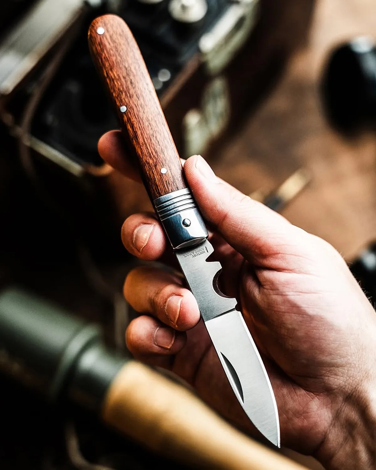 Hand holding a folding knife with a wooden handle and a partially serrated stainless steel blade.