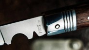 Close-up of a serrated knife blade with "HISTOR KNIFE & TOOL" engraved near a polished metal bolster and wooden handle.