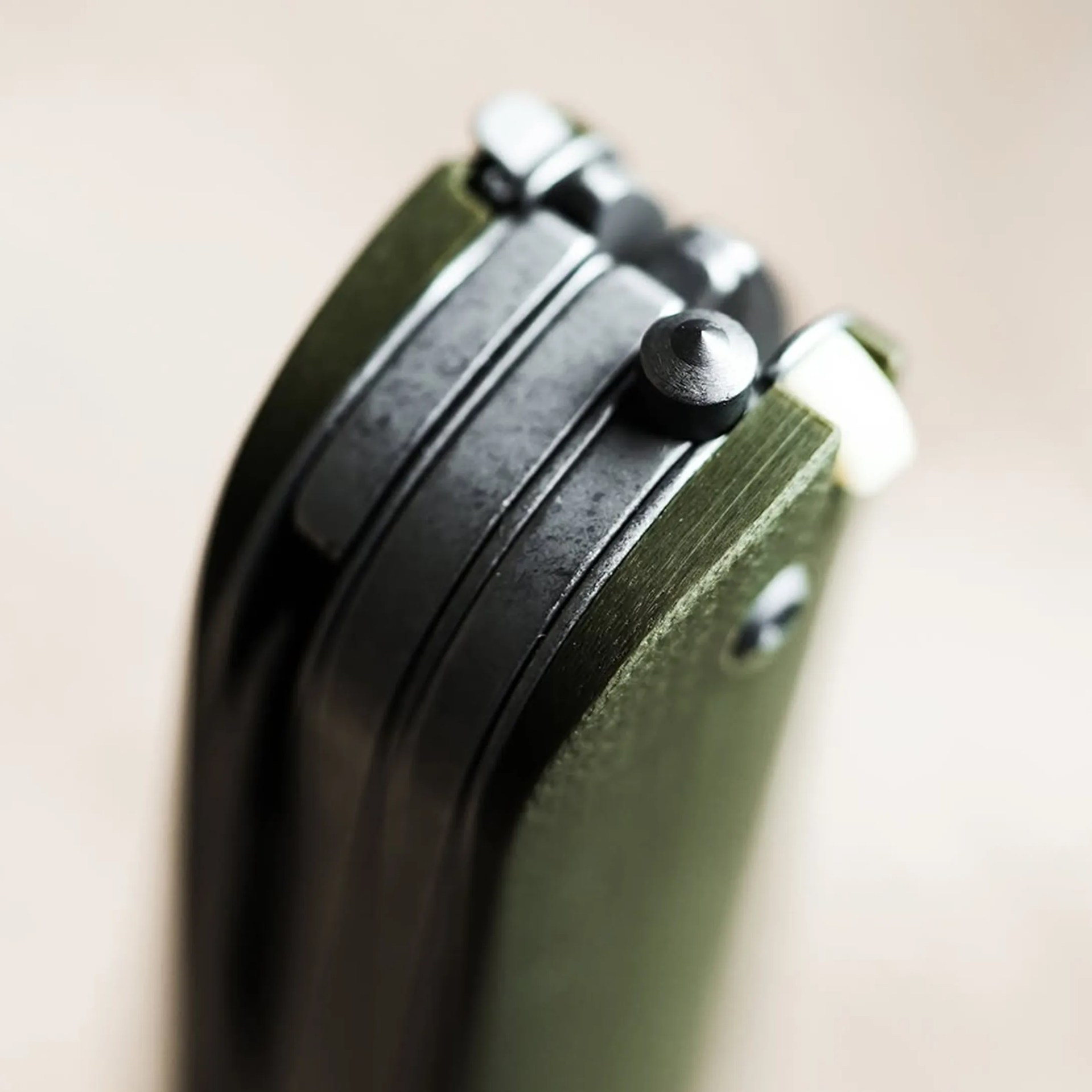 Close-up of a green and black folding knife hinge with a textured grip and metal components.