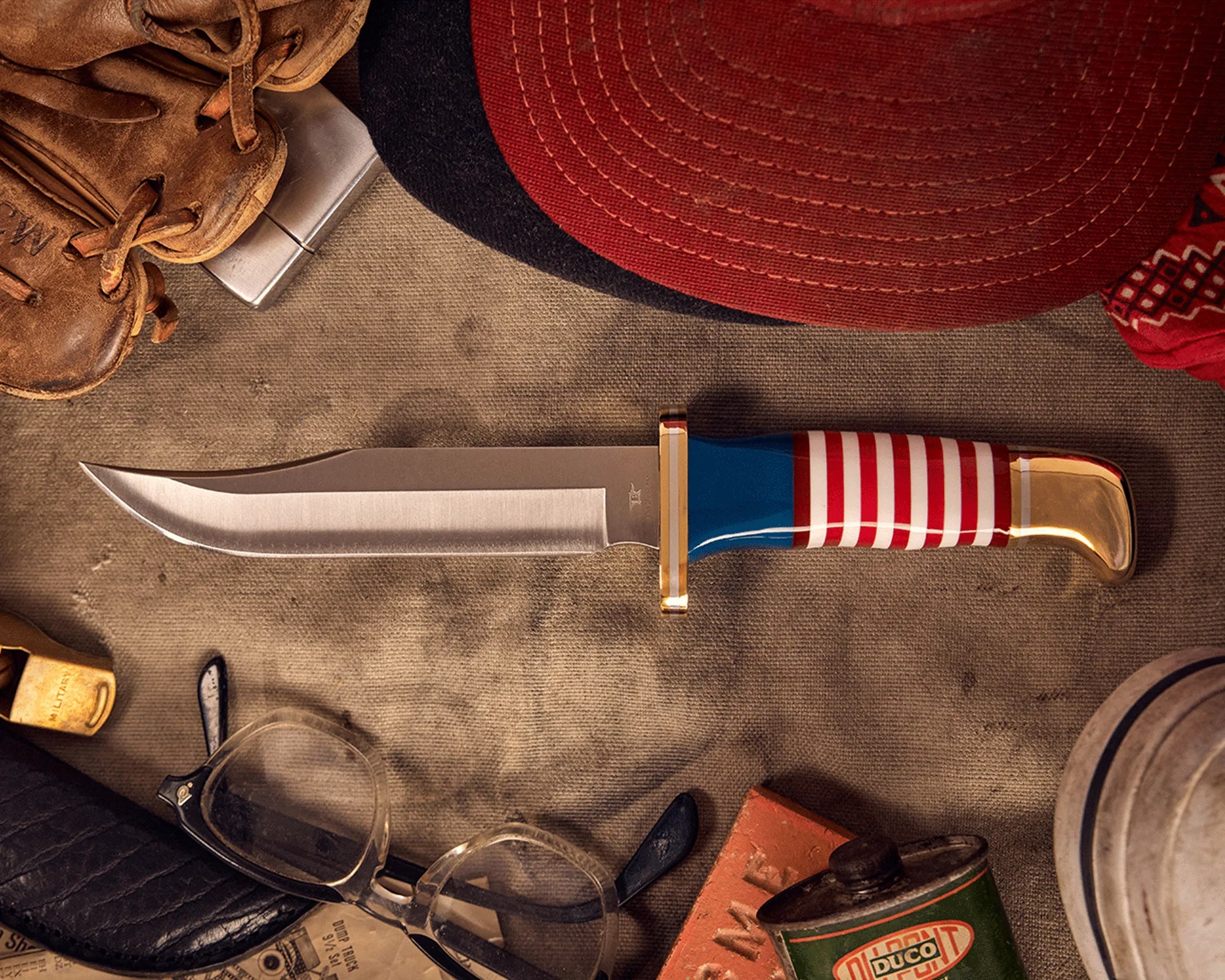 Knife with a polished blade and handle featuring red and white stripes and blue section, surrounded by vintage items on a textured surface.