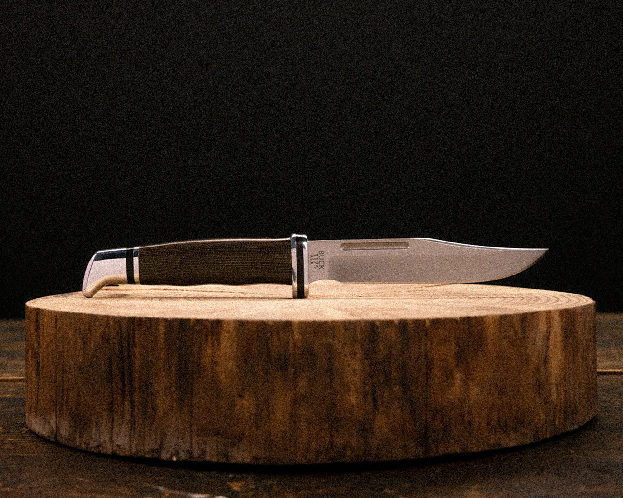 Fixed-blade knife with a wooden handle and polished metal bolster resting on a round wooden block.