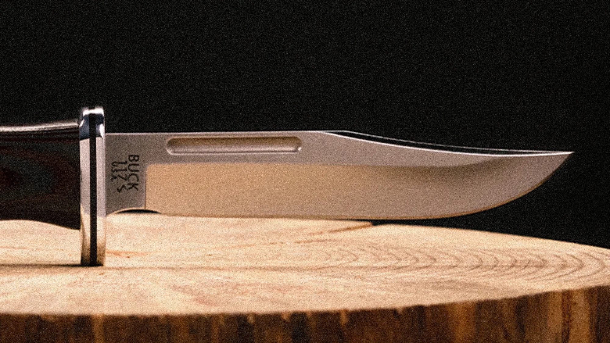 Close-up of a Buck USA fixed blade knife with a polished steel blade resting on a wooden surface.