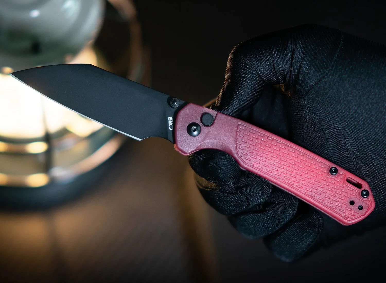 Black blade folding knife with textured red handle held in a gloved hand.