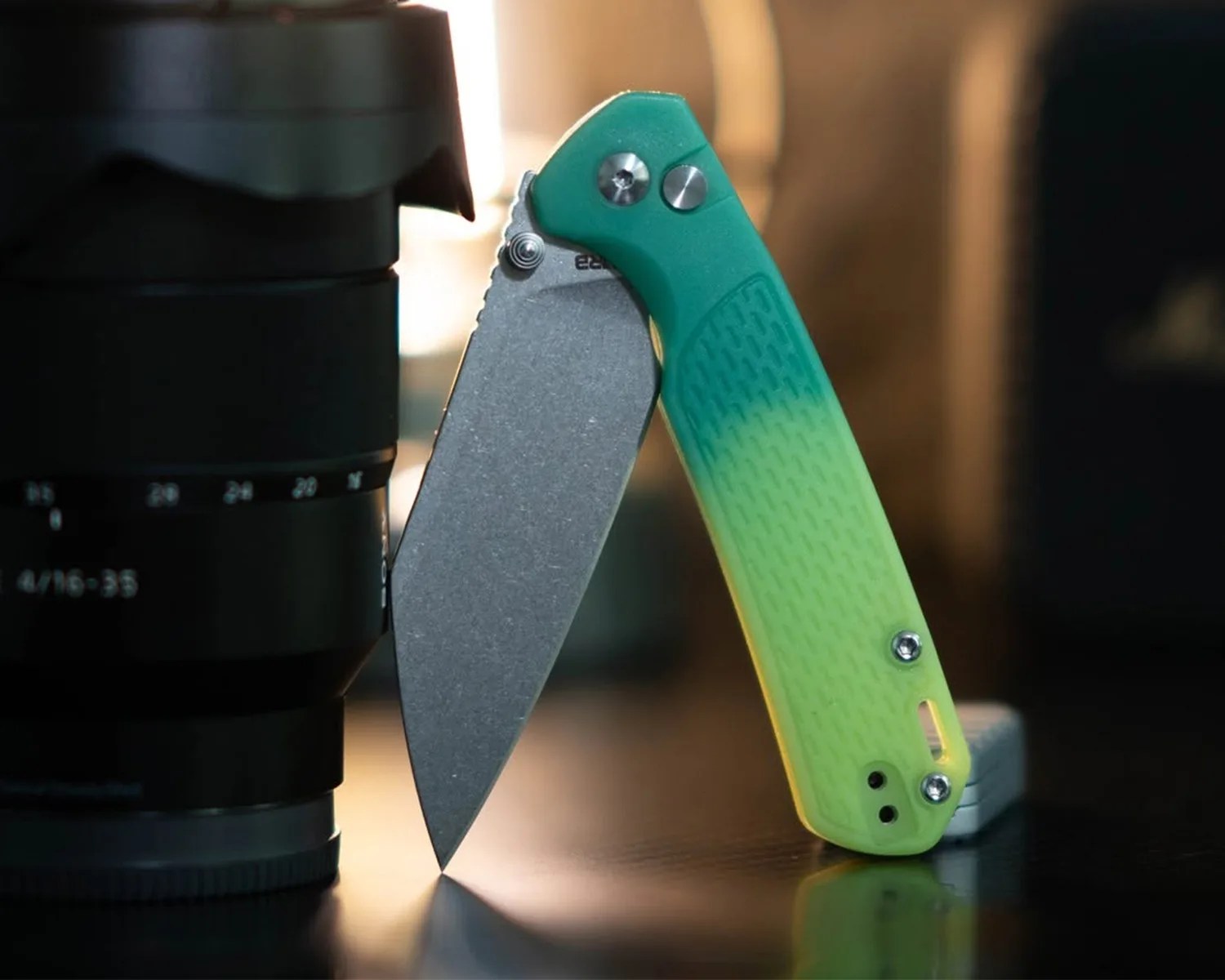 Folding knife with a stonewashed blade and green-to-yellow gradient textured handle standing open on a reflective surface.