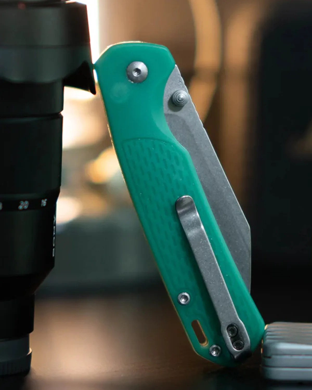 Green folding pocket knife with textured handle and metal clip standing upright on a dark surface.