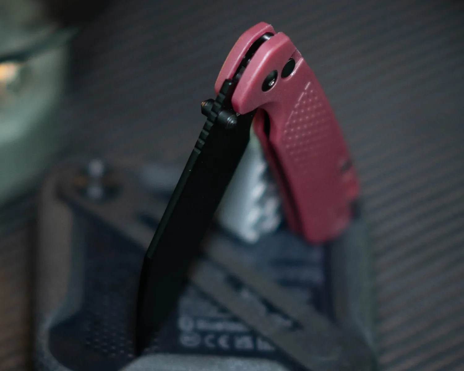 Black folding knife with a partially serrated blade and red textured handle.