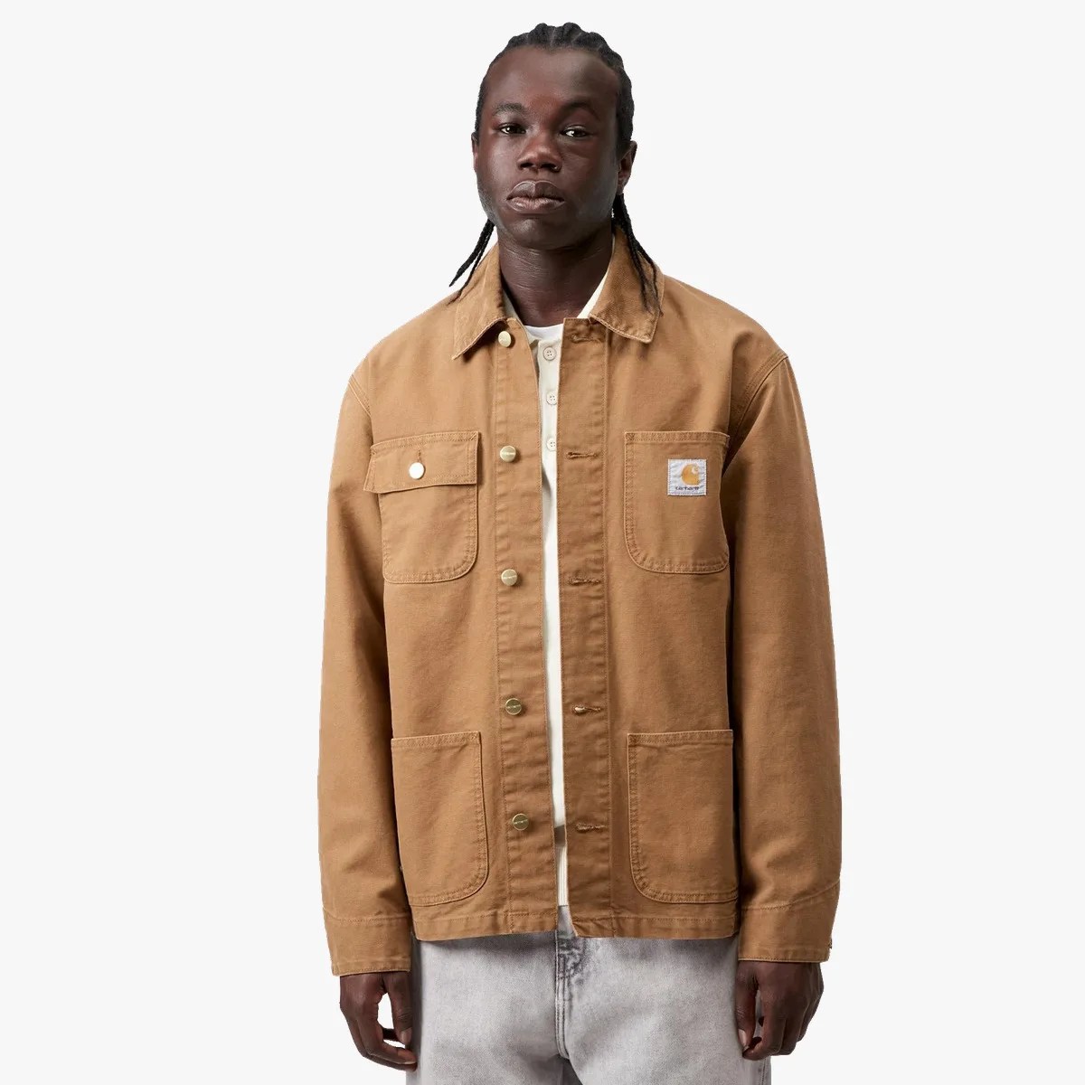 Brown Carhartt work jacket with four front pockets and snap buttons worn by a person.