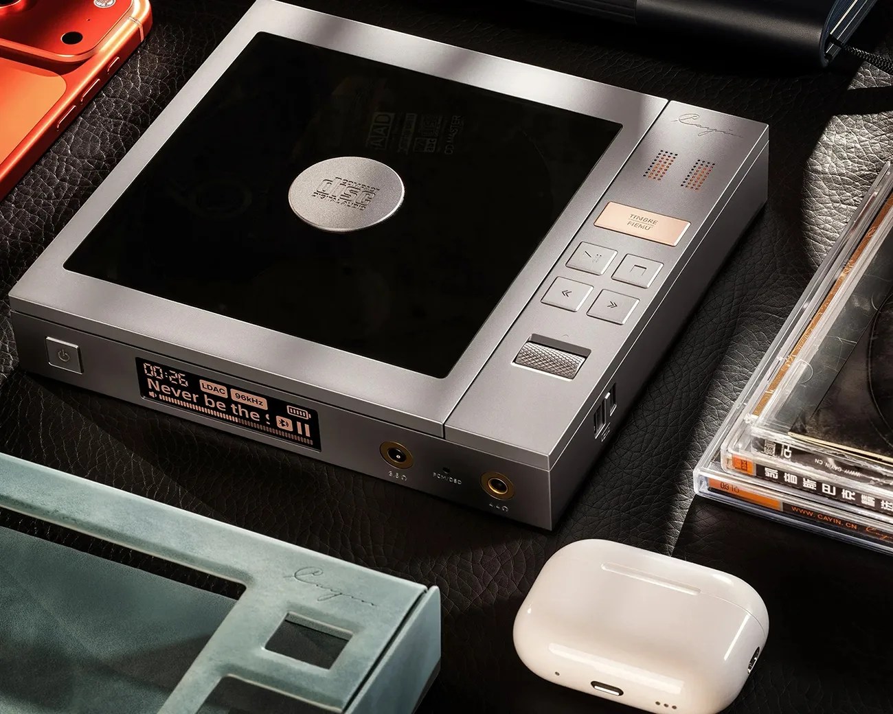 Silver digital audio player with a black display screen, control buttons, and a volume wheel on a black textured surface.