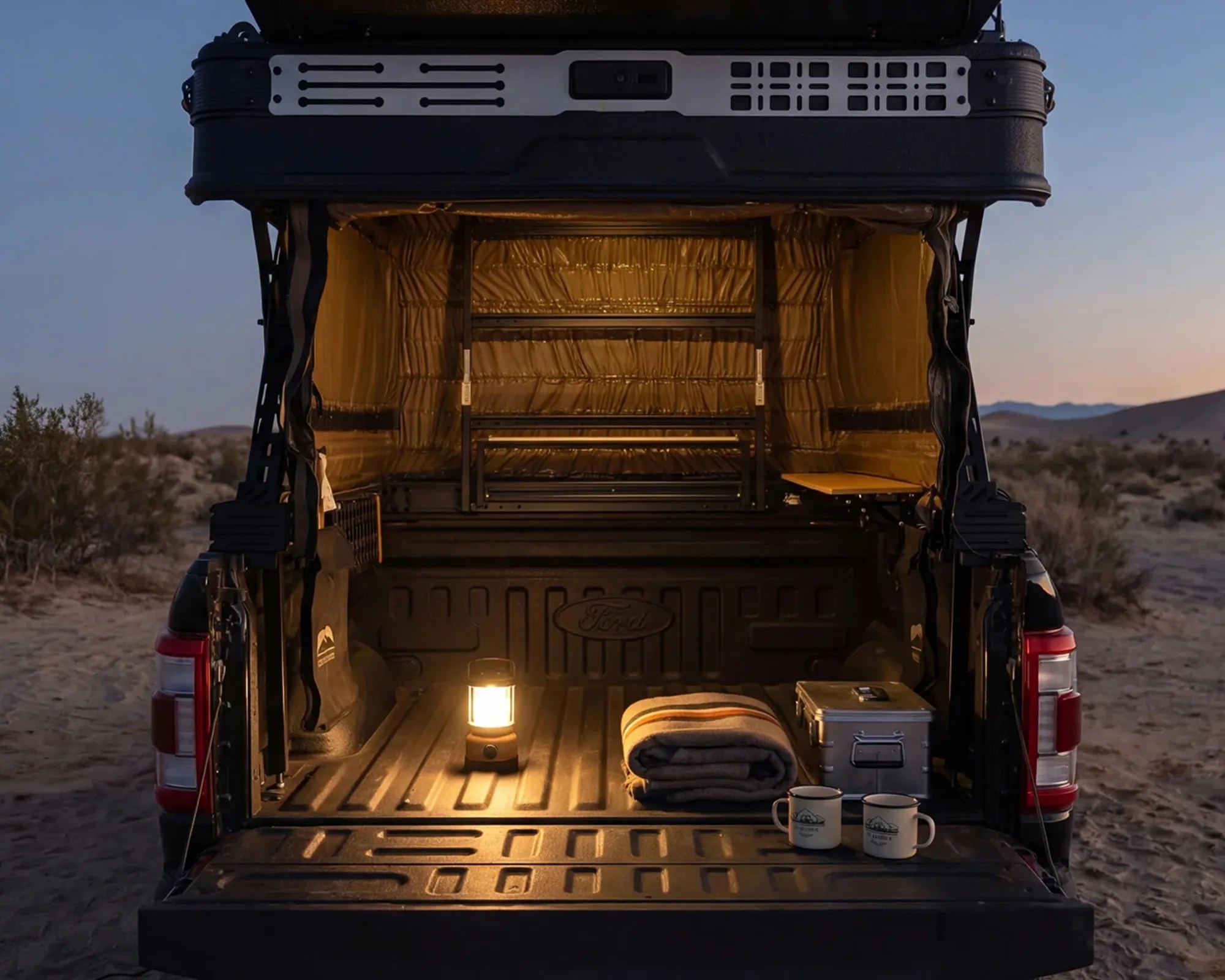 Open black truck bed with a lit lantern, folded blanket, metal box, and two enamel mugs at dusk.