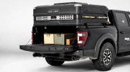 Black pickup truck with open tailgate carrying two metal storage boxes and a large black rooftop cargo box labeled "WILD LAND.
