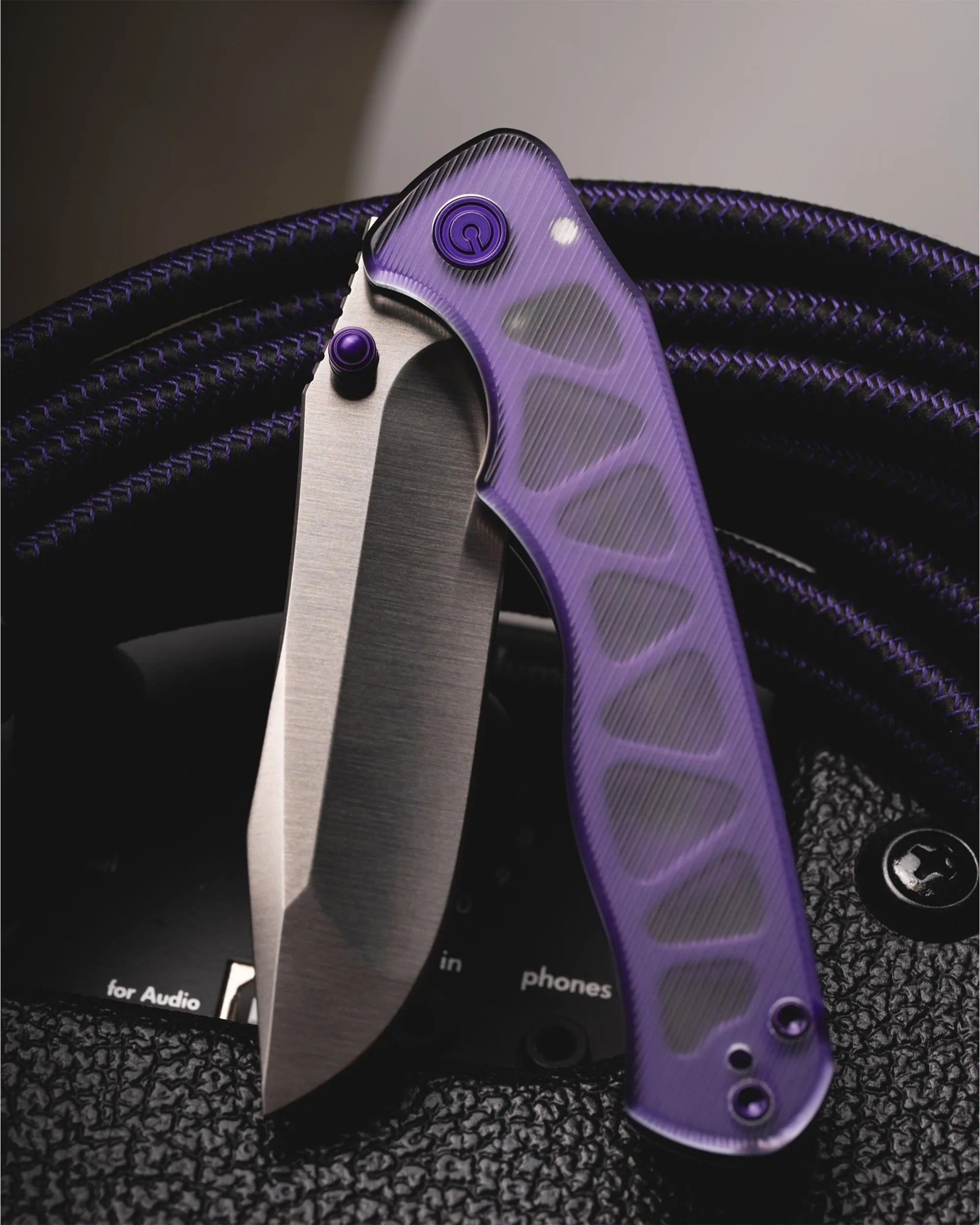 Folding knife with a purple textured handle and partially visible stainless steel blade on black textured surface.