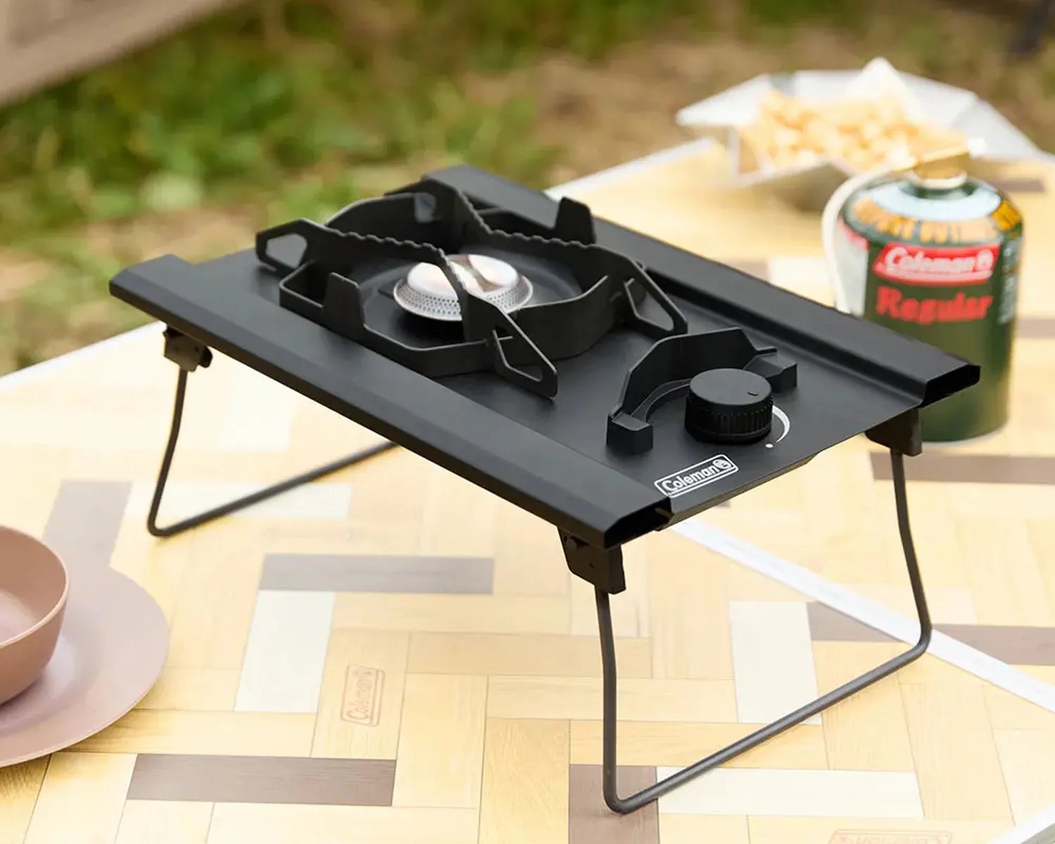 Black Coleman portable single-burner camping stove with foldable legs on a wooden table.
