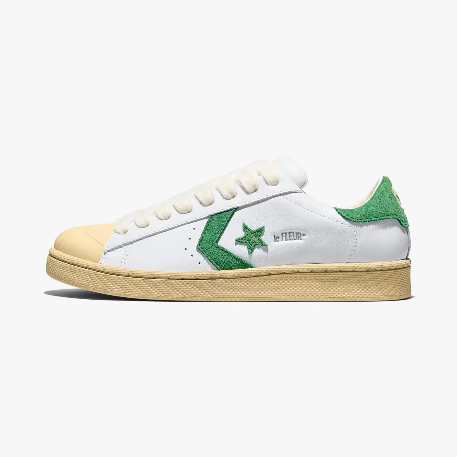 White leather sneaker with green suede star and heel tab, beige sole, and beige toe cap.