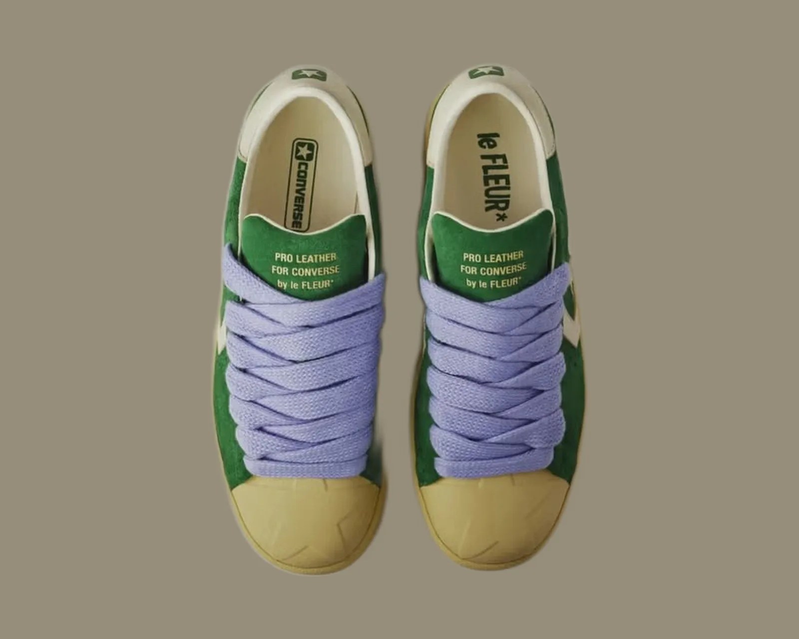 Pair of green Converse Pro Leather sneakers with beige toe caps and thick lavender laces on a beige background.