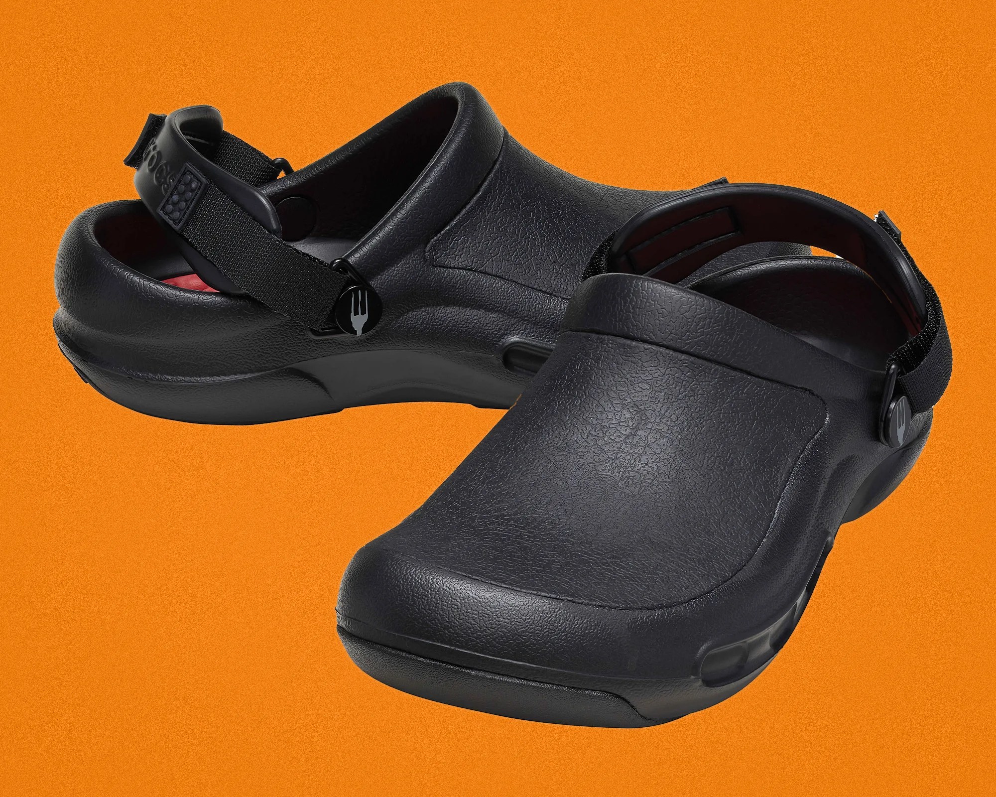 Pair of black slip-on clogs with adjustable heel straps on an orange background.