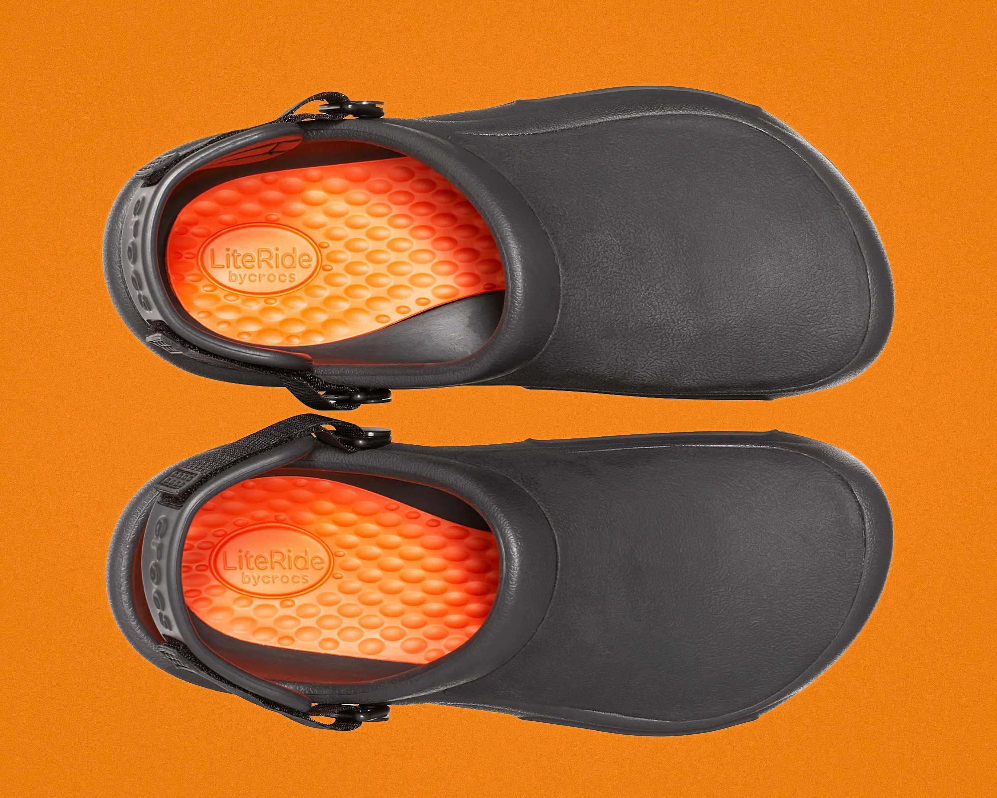 Pair of black Crocs clogs with bright orange LiteRide cushioned insoles on an orange background.