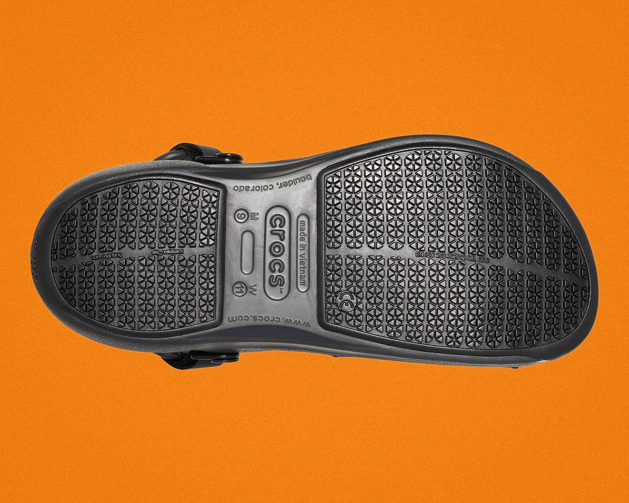 Black Crocs shoe sole with textured grip pattern on an orange background.