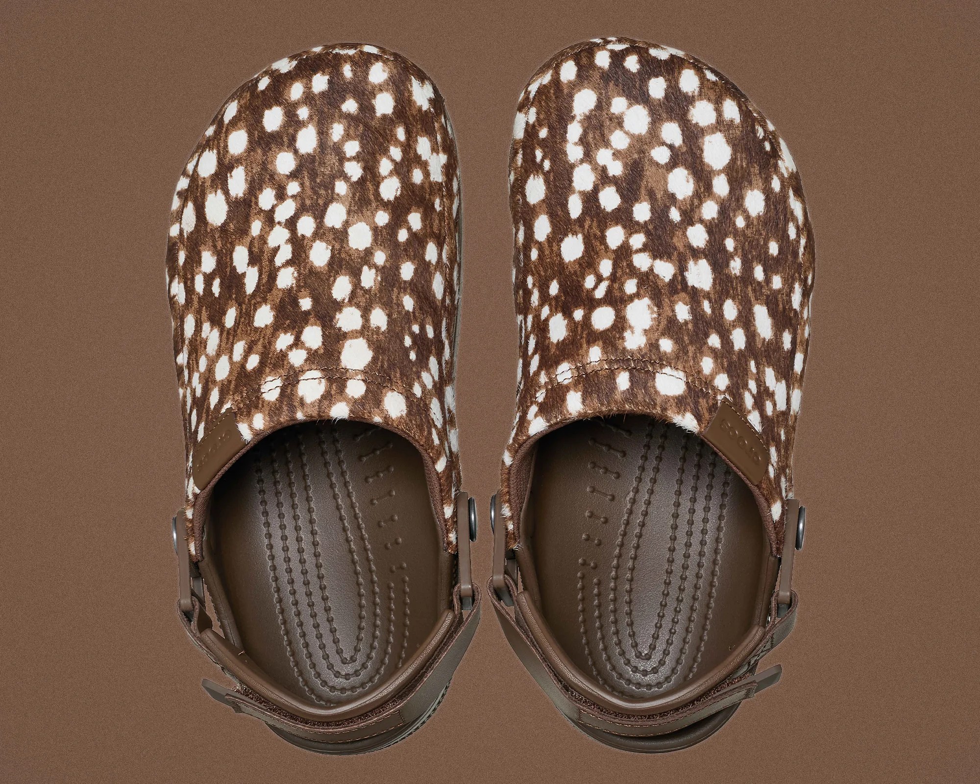 Pair of brown clogs with white spotted pattern and adjustable heel straps on a brown background.