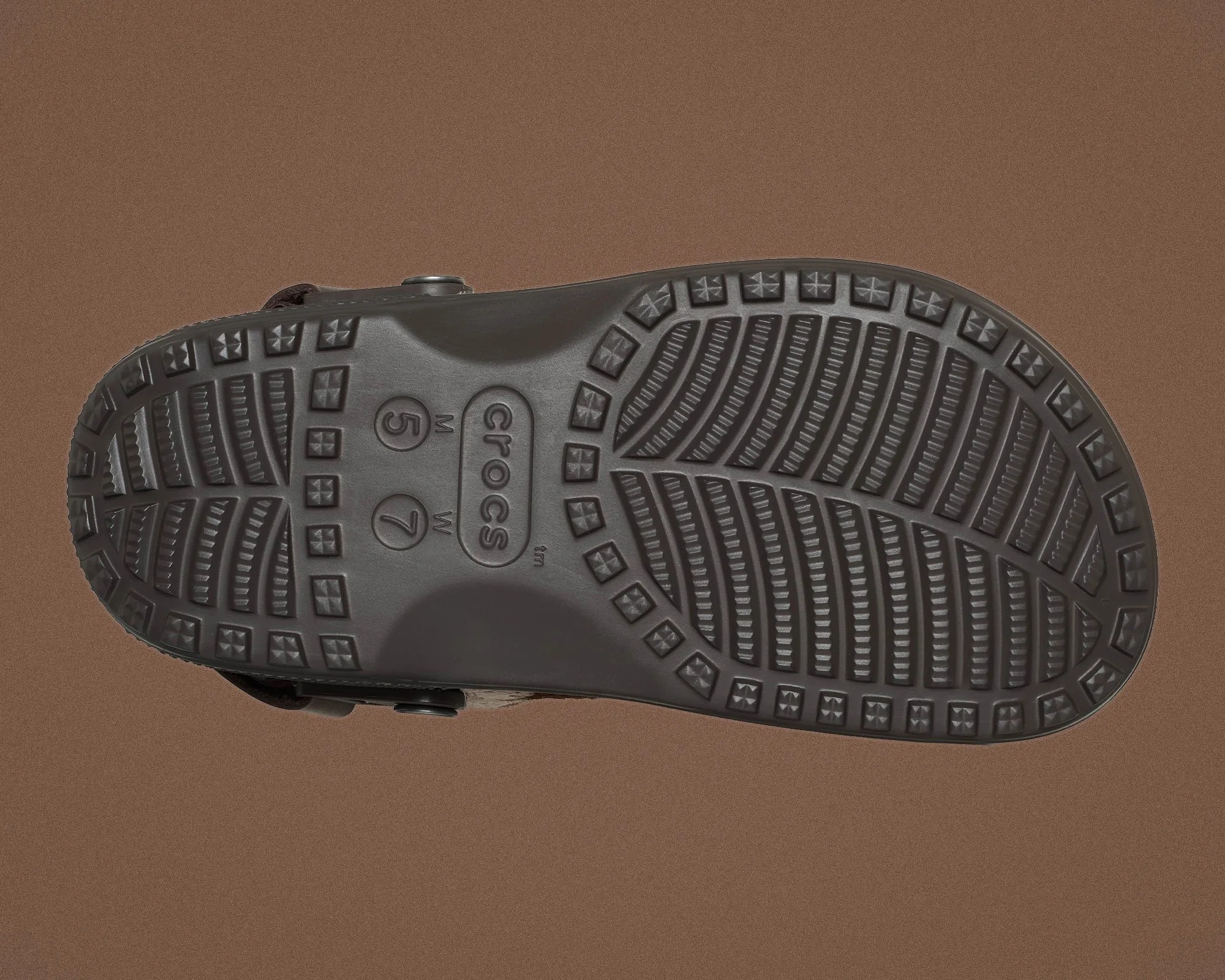 Black Crocs shoe sole with textured tread pattern on a brown background.