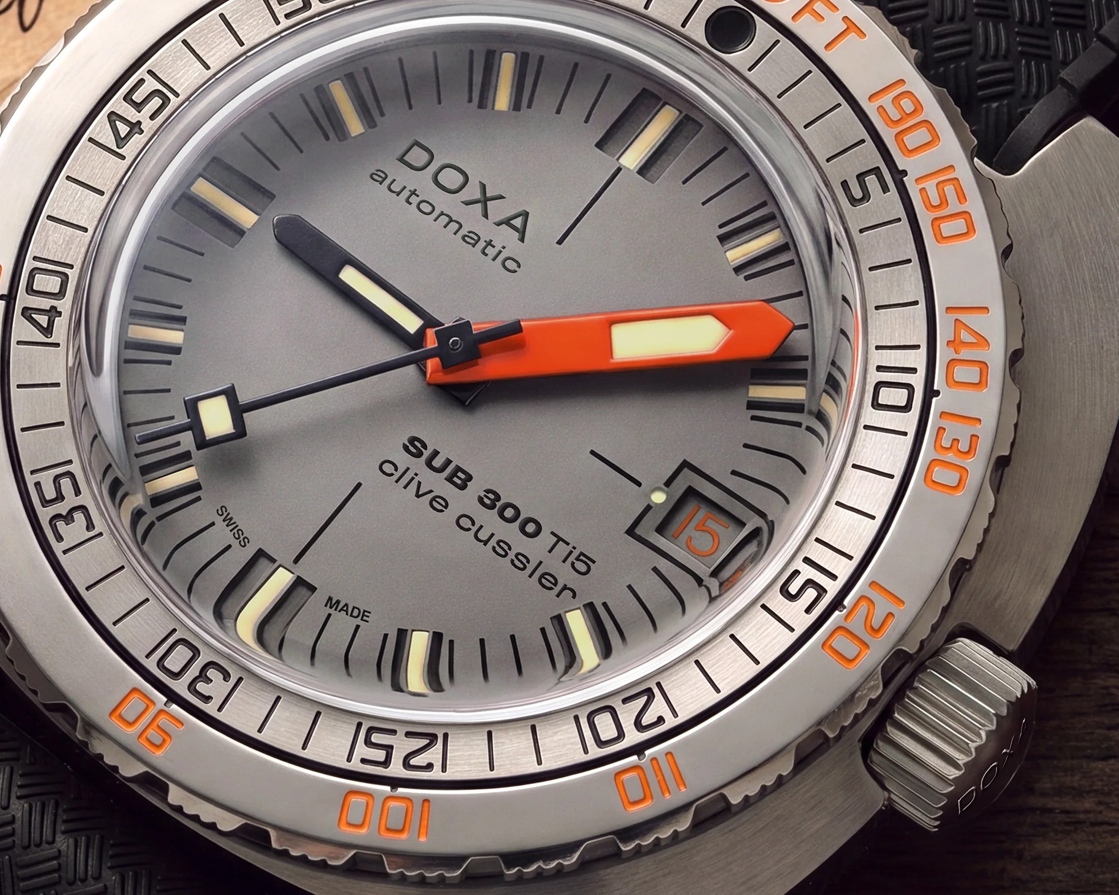 Close-up of a DOXA SUB 300 Ti5 dive watch with orange and black hands and a date window showing the 15th.