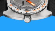 Close-up of a stainless steel watch case with a knurled crown engraved with "DOXA" and an orange-accented bezel.
