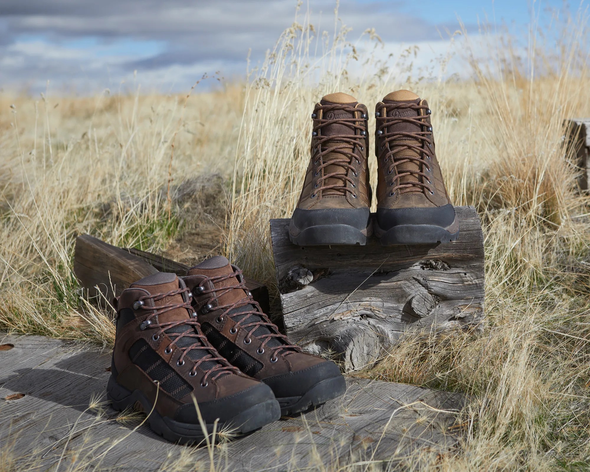 Pair of brown leather hiking boots on a wooden surface with dry grass in the background.