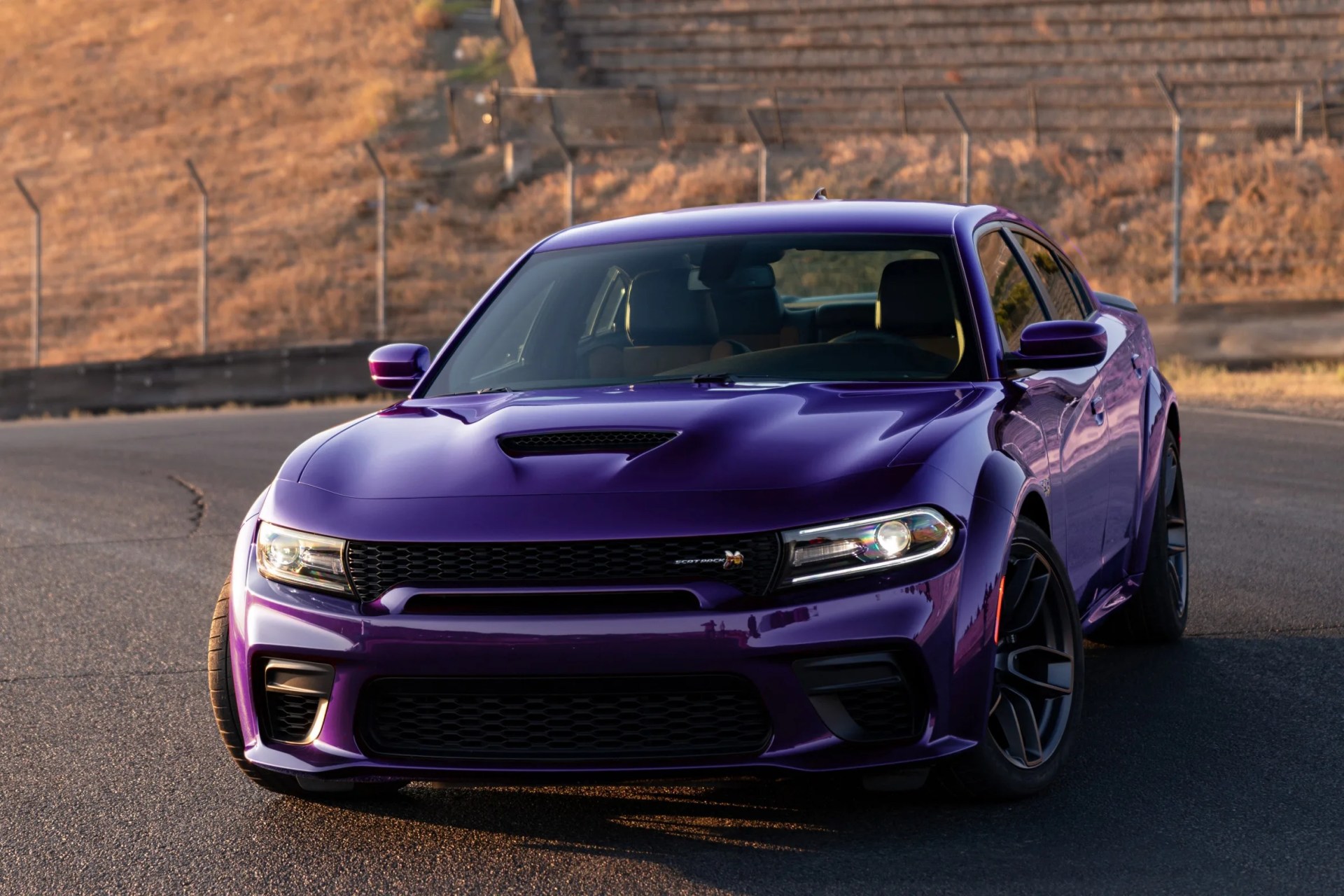 Purple Dodge Charger SRT Hellcat with black grille and hood scoop on a paved road.
