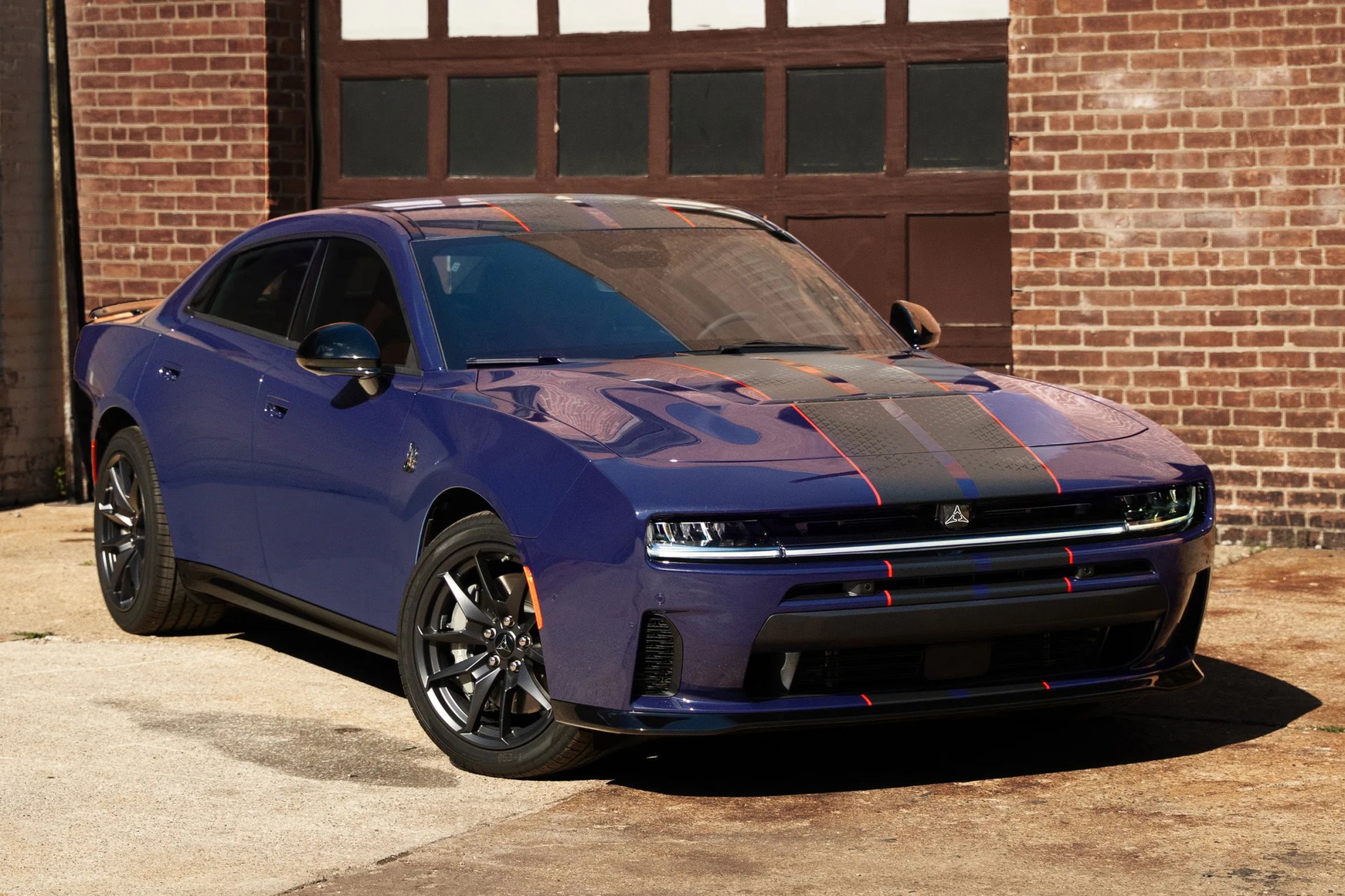 Blue electric sedan with black and red racing stripes parked in front of a brick building.