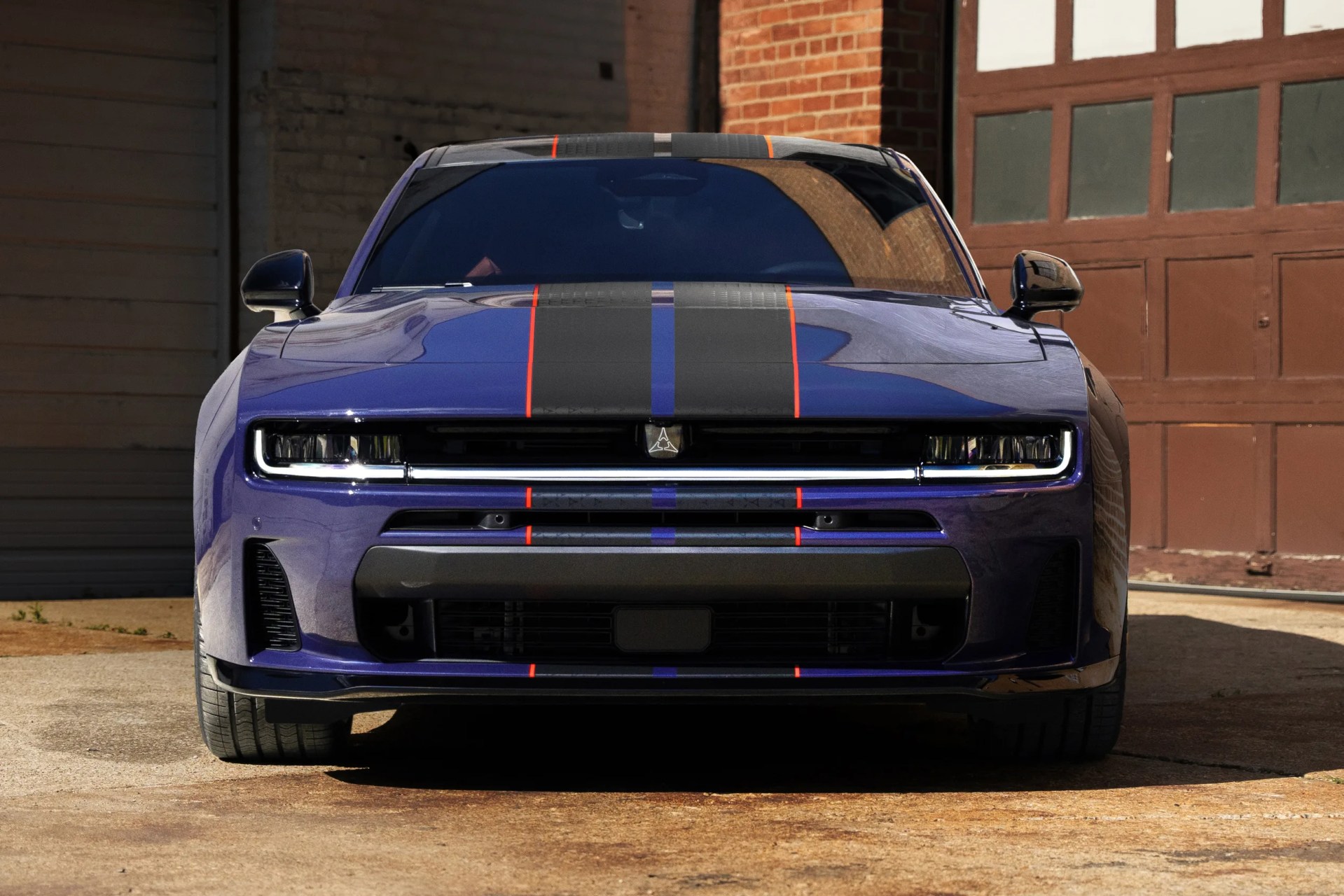 Front view of a blue car with black and orange racing stripes parked in front of a brick building.