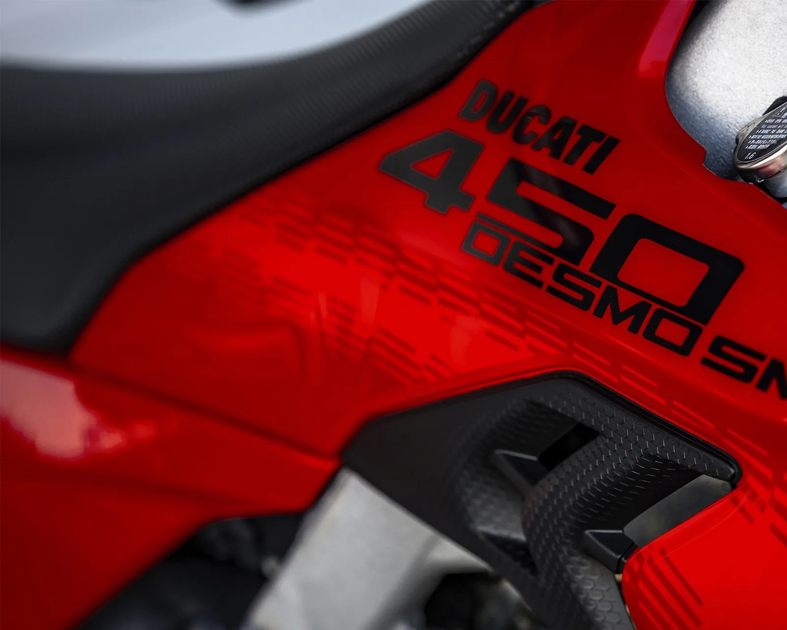 Close-up of red Ducati 450 Desmo motorcycle fuel tank with black textured grip pad.