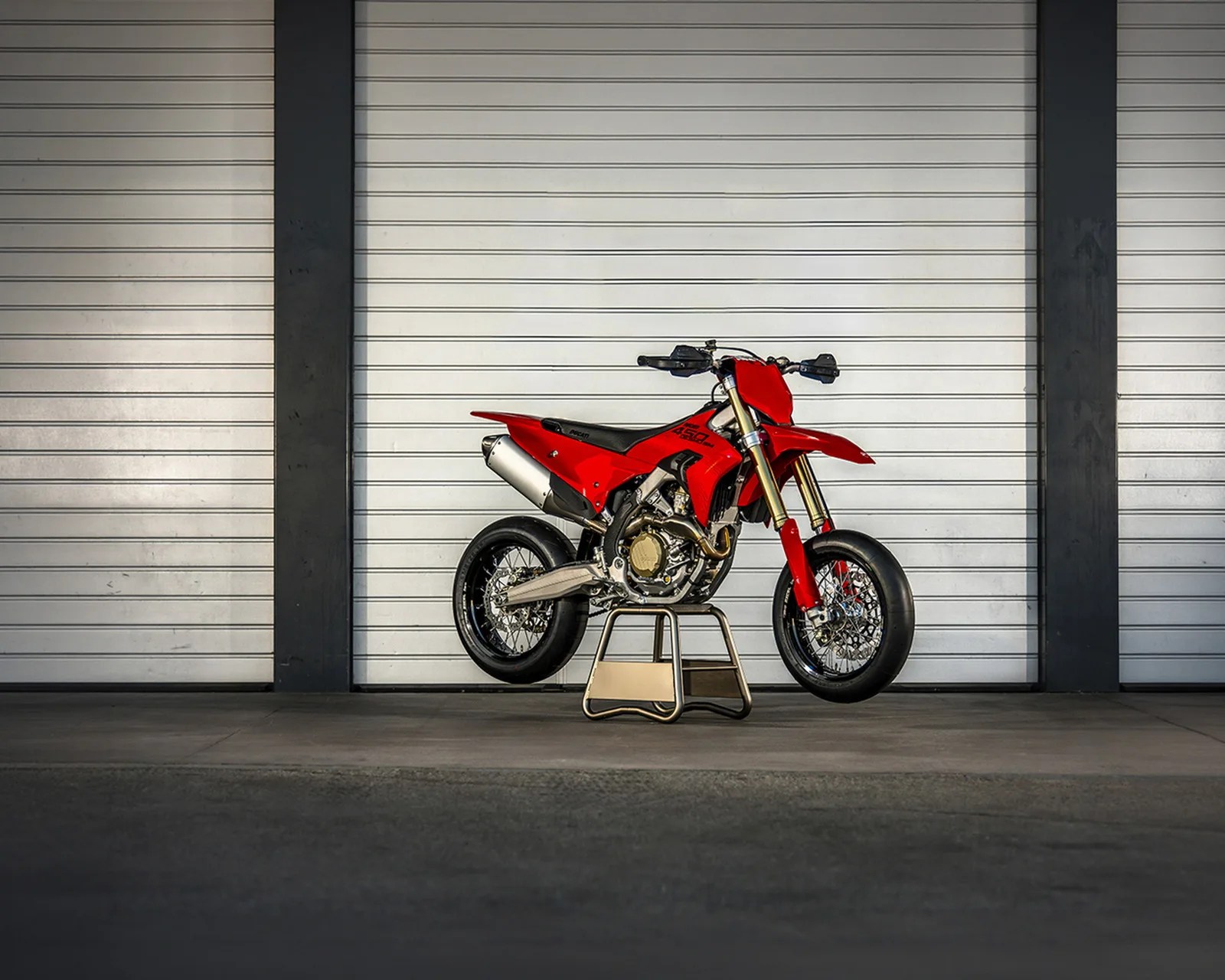 Red Ducati 450 SM motorcycle on a stand in front of a white metal garage door.