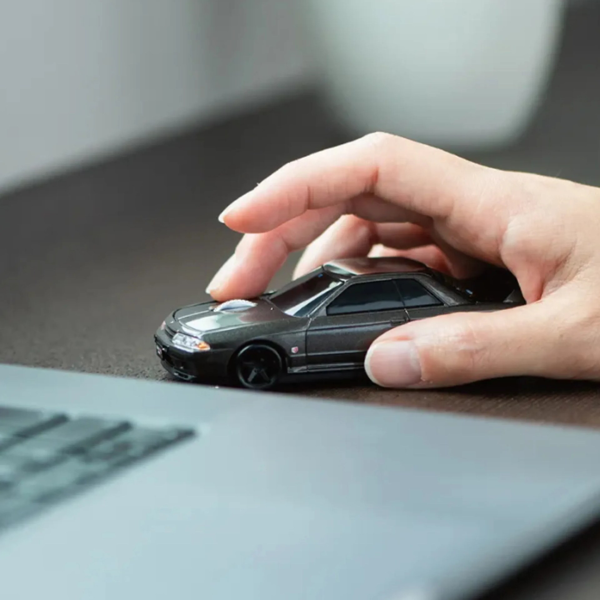 Hand holding a black toy car on a dark surface near a blurred laptop keyboard.