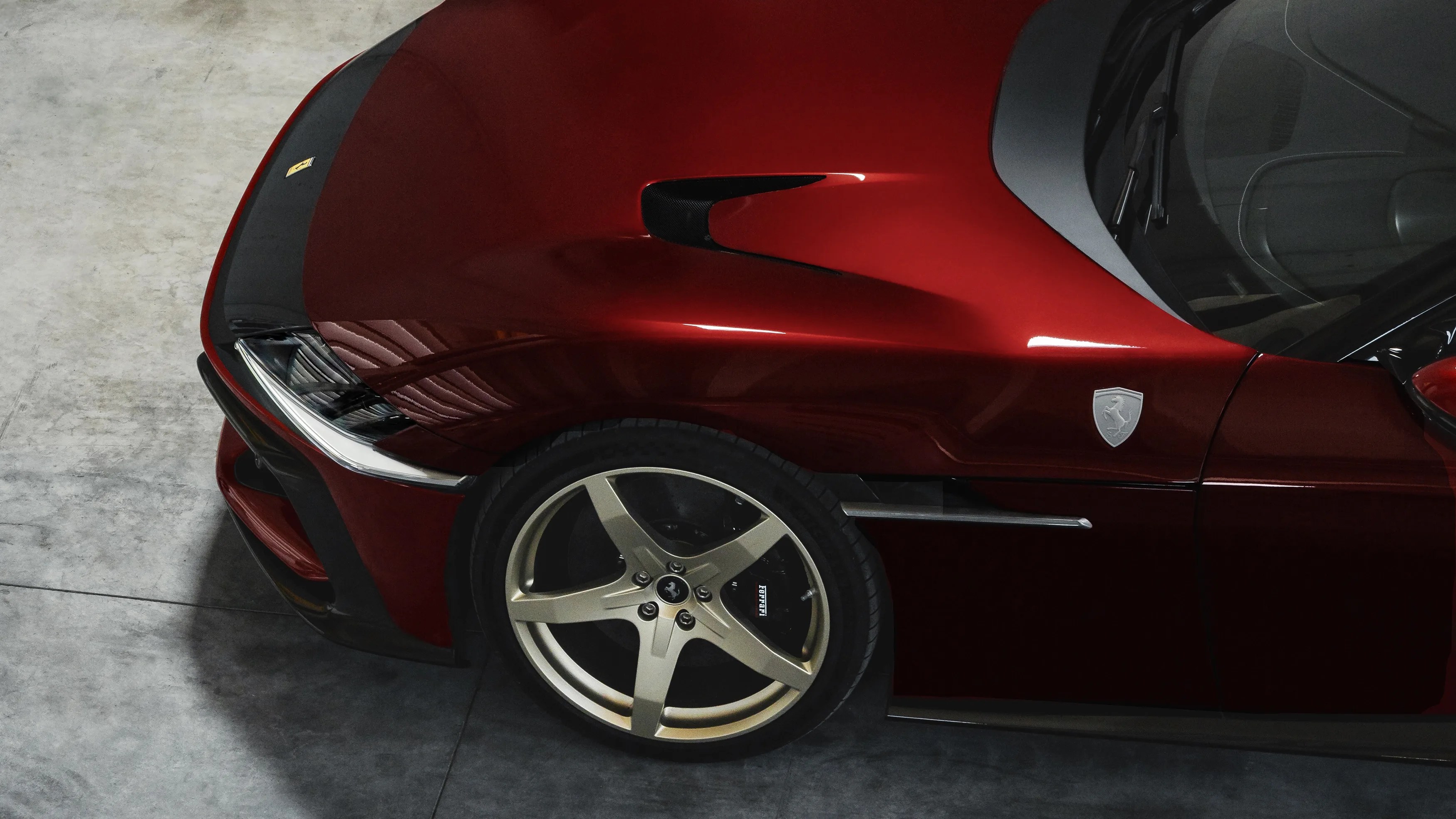 Close-up of the front left side of a glossy red Ferrari with silver five-spoke wheel and black brake caliper.