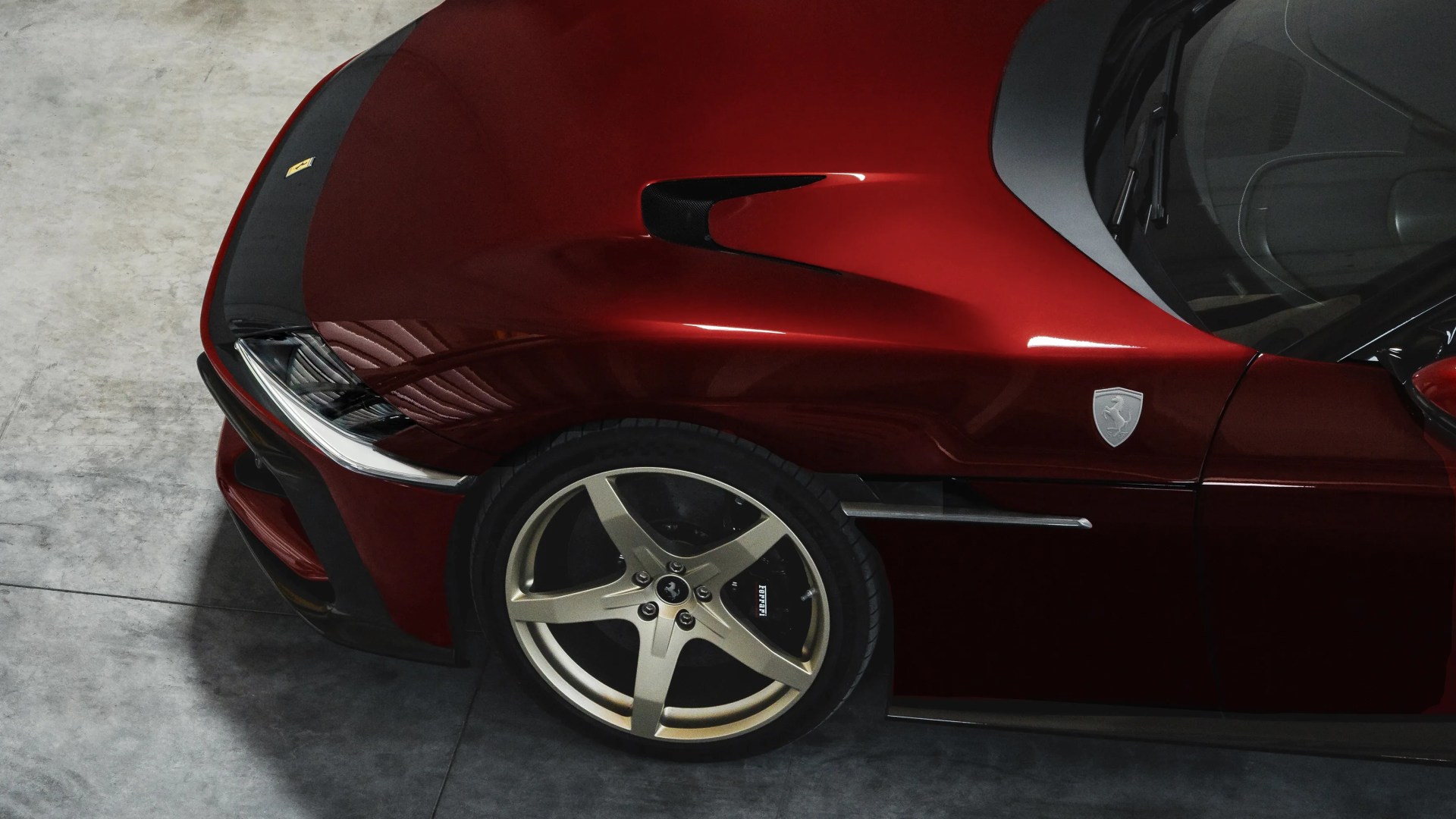 Close-up of the front left side of a glossy red Ferrari with silver five-spoke wheel and black brake caliper.