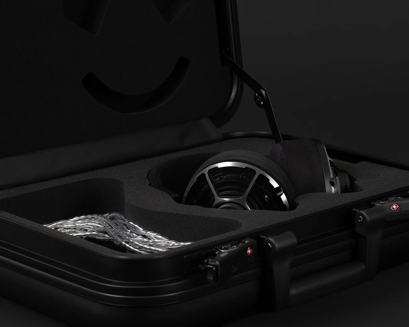Black hard case with foam interior holding a pair of black and silver headphones and a coiled silver cable.