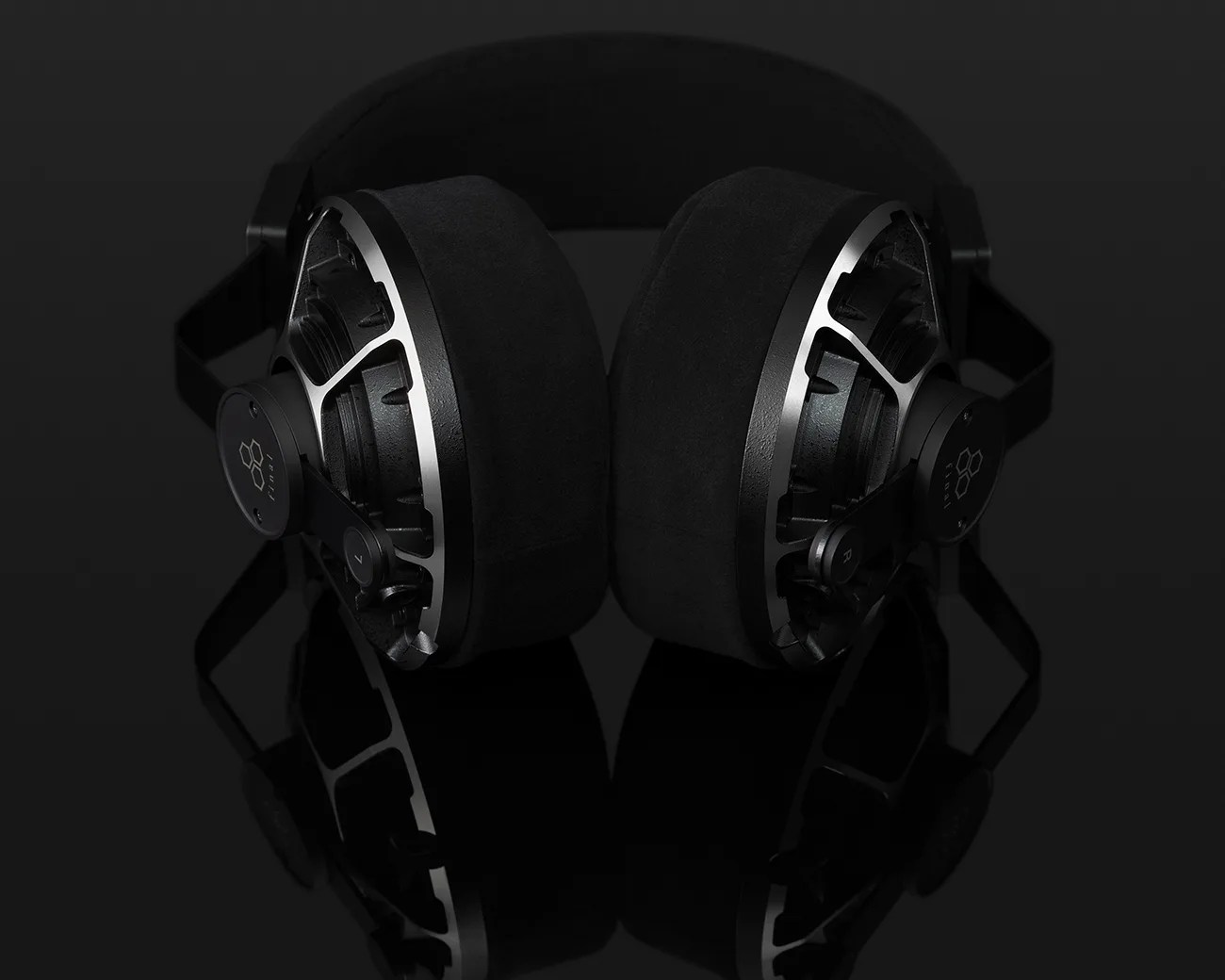 Black over-ear headphones with metal frame and thick cushioned ear pads on a reflective black surface.