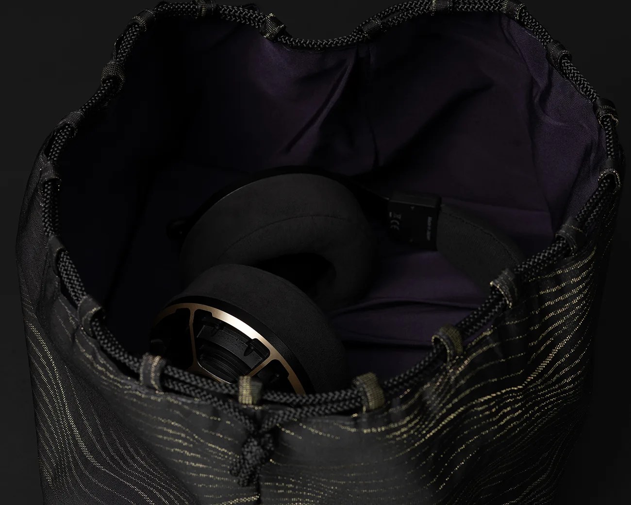 Black and gold over-ear headphones inside a black drawstring bag with gold stitching.