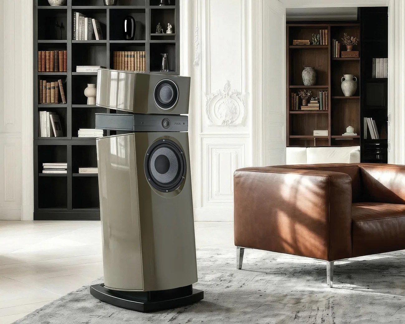 Glossy beige floor-standing speaker with two visible drivers on a gray rug in a modern living room.