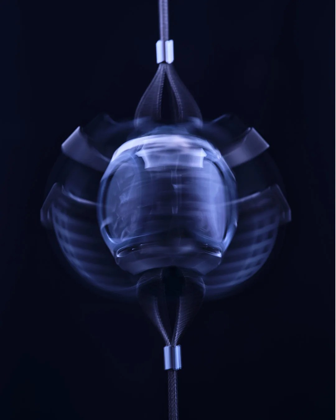 Suspended glass object spinning rapidly against a dark background, creating a blurred motion effect.