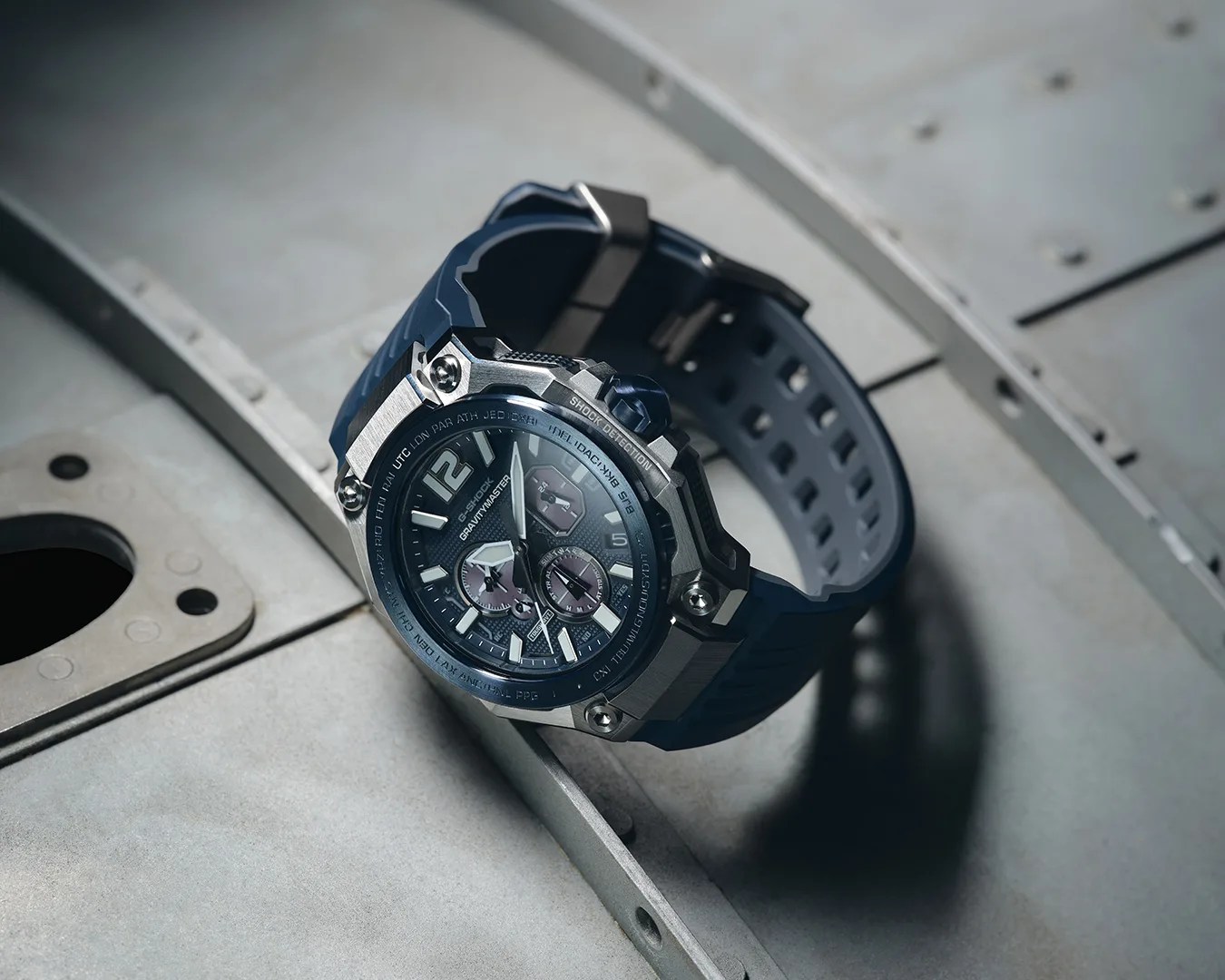 Blue G-Shock Gravitymaster watch with silver bezel and multiple dials on a metal surface.