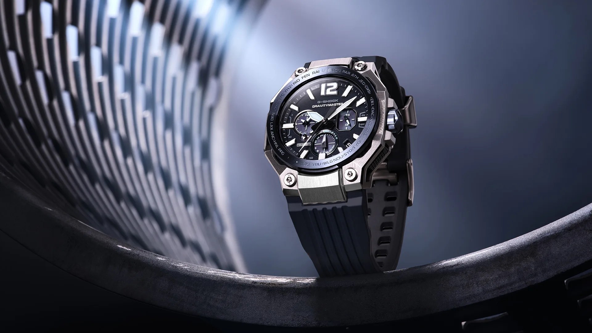Black G-Shock Gravitymaster watch with silver bezel and black rubber strap on a curved metallic surface.