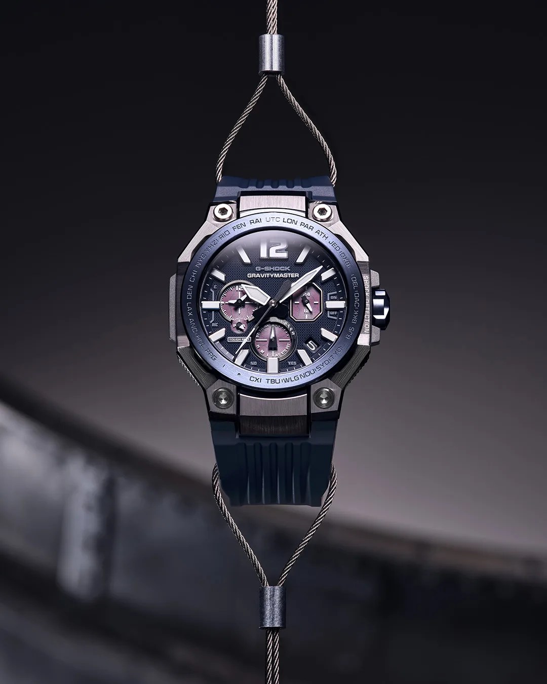 Blue G-Shock Gravitymaster watch with metal case and multiple dials, suspended by steel cables.
