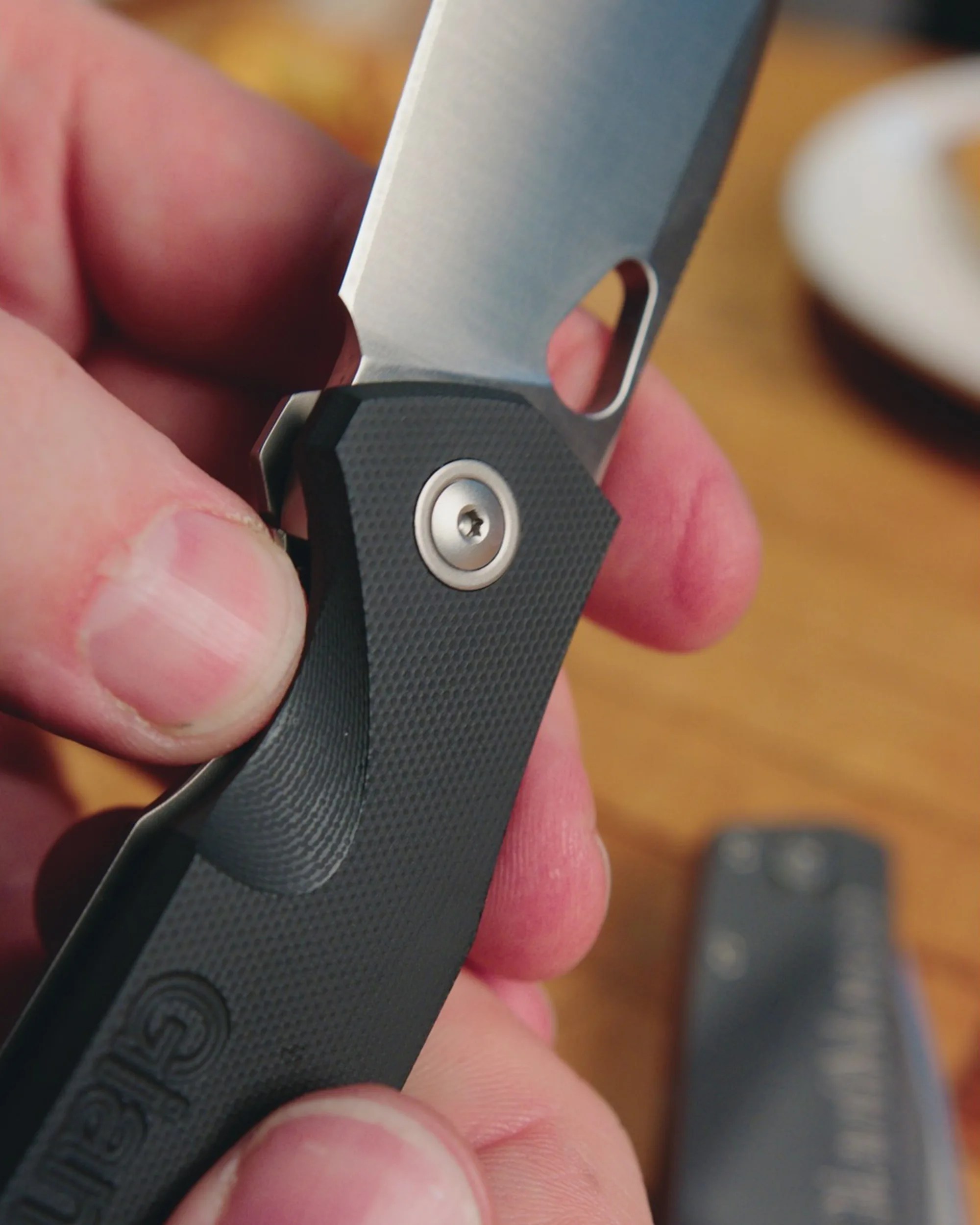 Hand holding a black textured folding knife with a partially open silver blade.