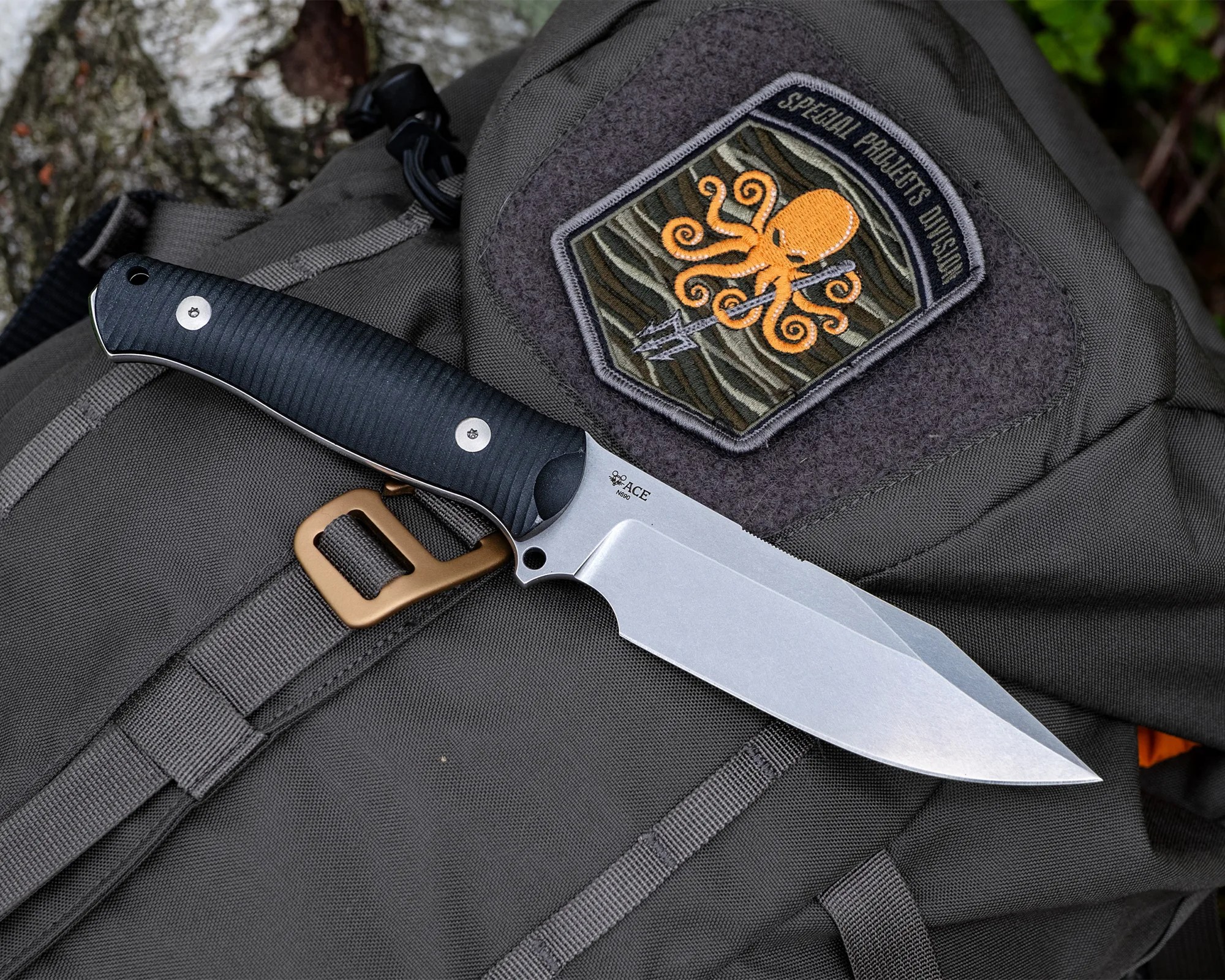 Knife with black textured handle and silver blade resting on a gray backpack with an orange octopus patch reading "Special Projects Division.