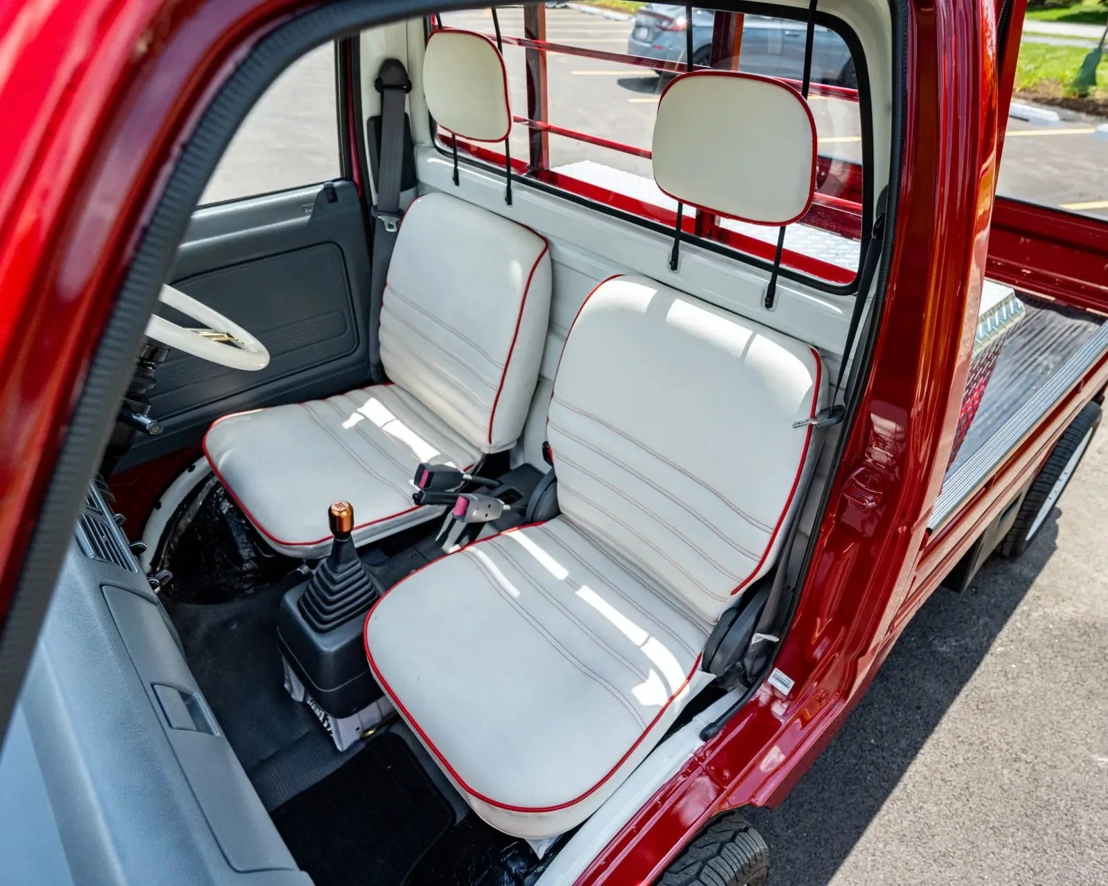 Interior of a red vehicle with two white seats outlined in red piping and a manual gear shift with a bronze knob.